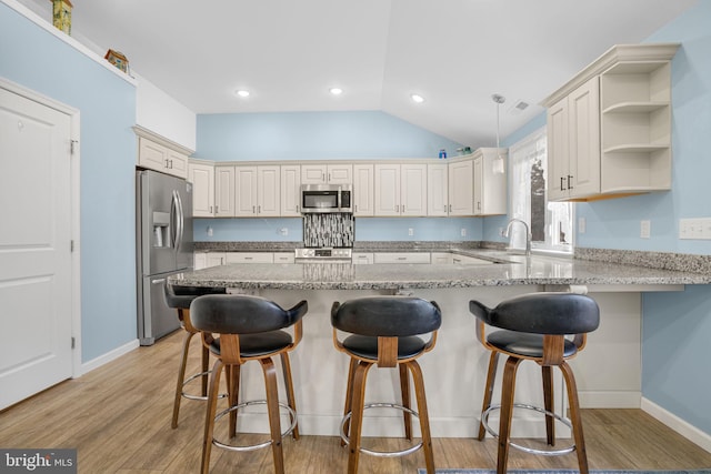 kitchen with appliances with stainless steel finishes, lofted ceiling, light wood-style floors, and a peninsula