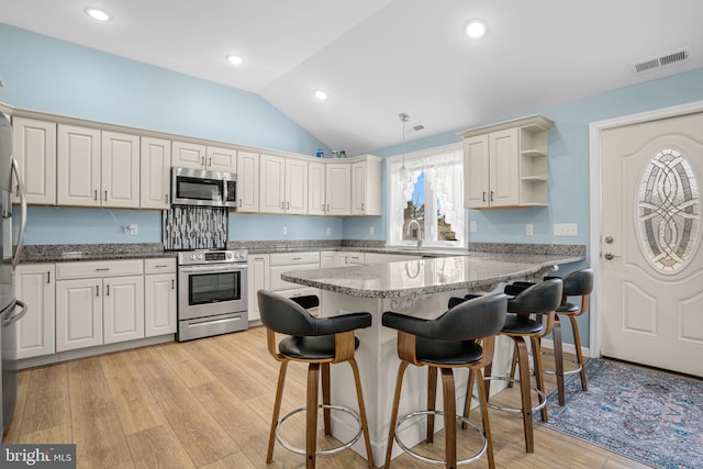 kitchen featuring a breakfast bar, lofted ceiling, visible vents, appliances with stainless steel finishes, and light wood-type flooring