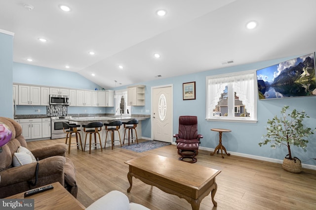 living area featuring light wood-style floors, baseboards, visible vents, and vaulted ceiling