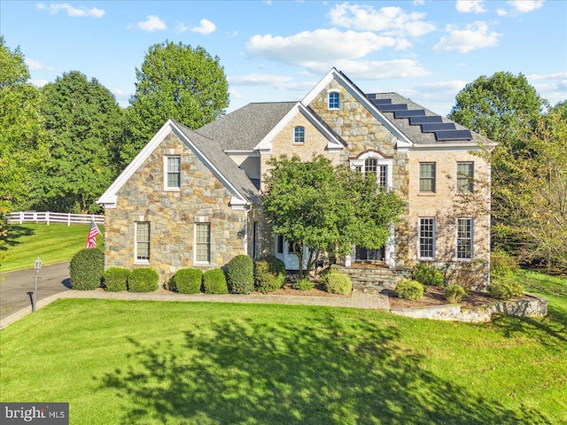 view of front of property featuring roof mounted solar panels, fence, and a front yard