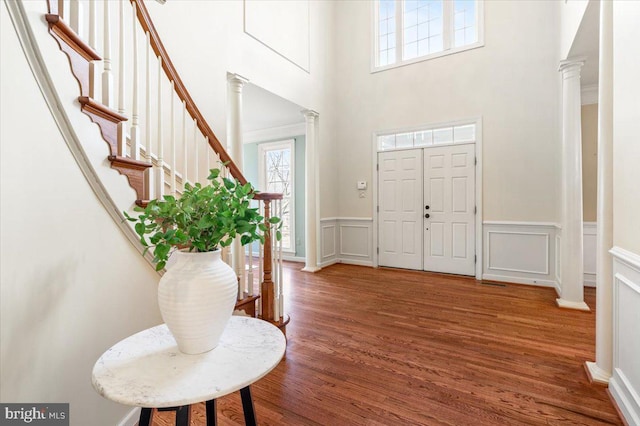 foyer entrance featuring stairs, a decorative wall, ornate columns, and wood finished floors