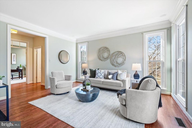 living room with ornamental molding, wood finished floors, visible vents, and baseboards