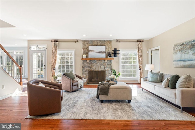 living area with stairs, a stone fireplace, wood finished floors, and baseboards