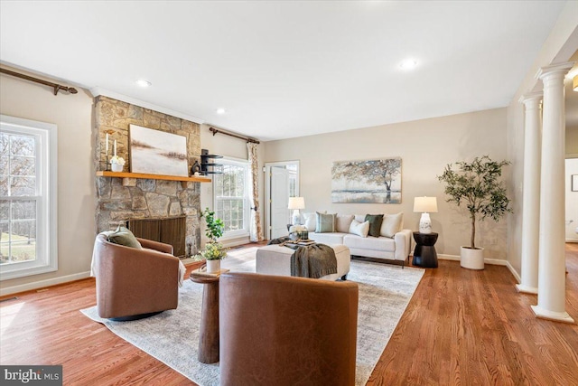 living room featuring a fireplace, decorative columns, baseboards, and wood finished floors