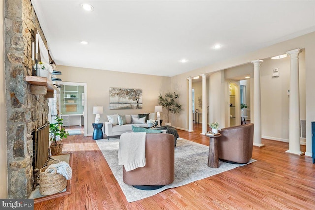 living room featuring a stone fireplace, wood finished floors, decorative columns, and recessed lighting