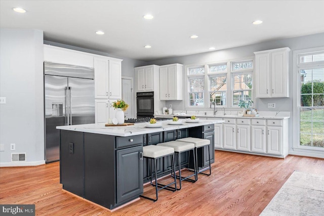 kitchen featuring visible vents, a breakfast bar, a center island, stainless steel built in fridge, and white cabinetry