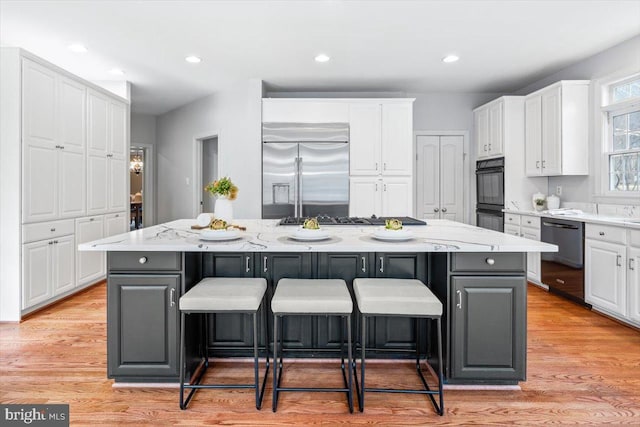 kitchen featuring a large island, a breakfast bar area, stainless steel appliances, light wood-style floors, and white cabinetry