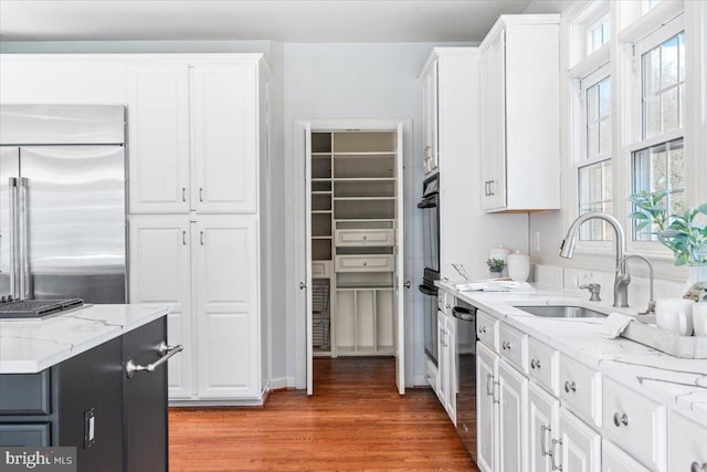 kitchen featuring appliances with stainless steel finishes, white cabinets, a sink, and light wood-style flooring