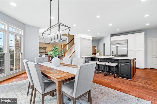 dining space with light wood-style floors, stairs, an inviting chandelier, and recessed lighting