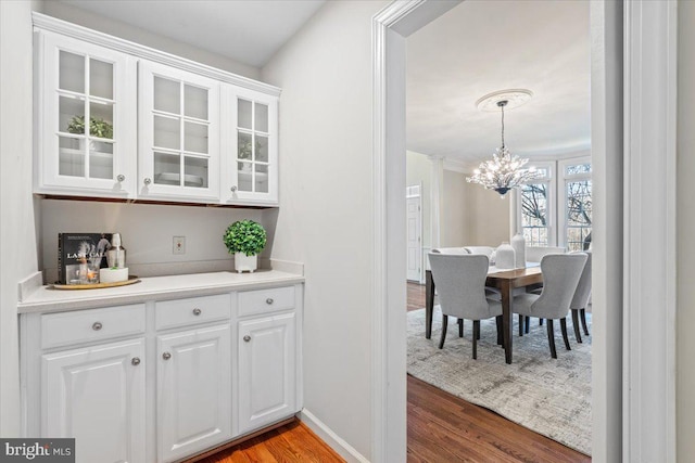 bar with pendant lighting, a notable chandelier, baseboards, and wood finished floors