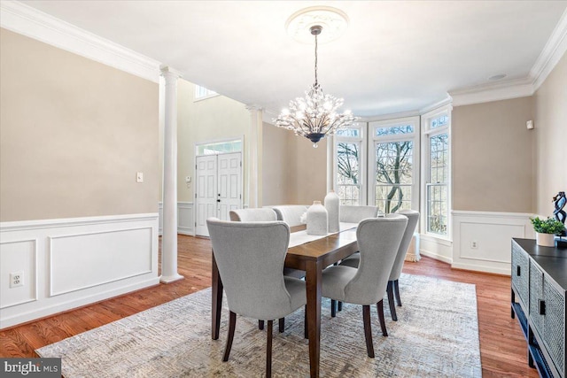 dining room featuring a healthy amount of sunlight, an inviting chandelier, wood finished floors, and ornate columns