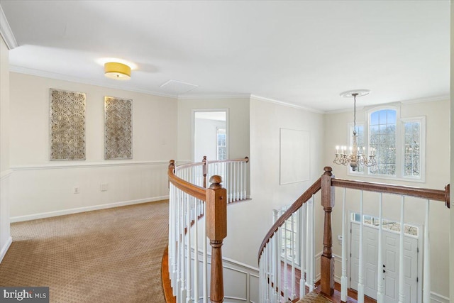 hall with a notable chandelier, carpet flooring, crown molding, and an upstairs landing