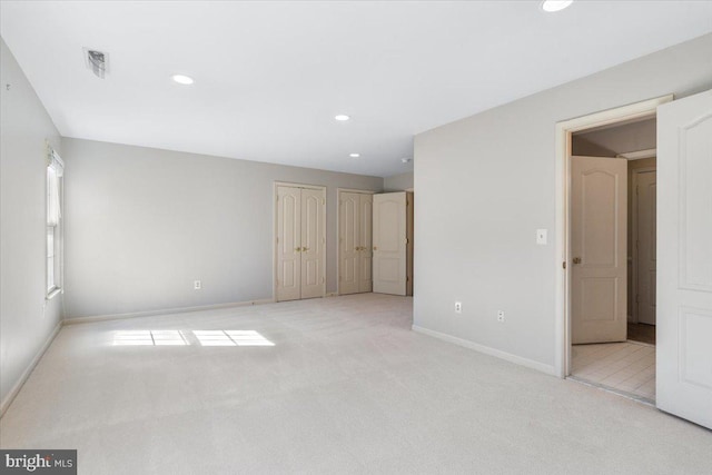 unfurnished bedroom featuring light carpet, recessed lighting, two closets, and baseboards