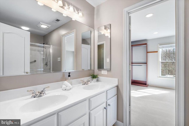 bathroom with double vanity, a shower with door, visible vents, and a sink