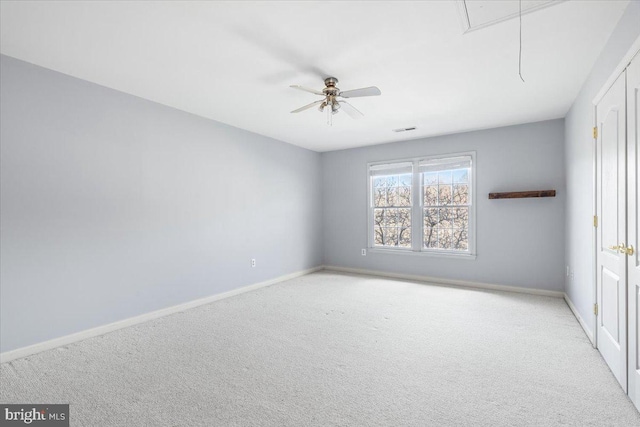 carpeted spare room with attic access, ceiling fan, and baseboards