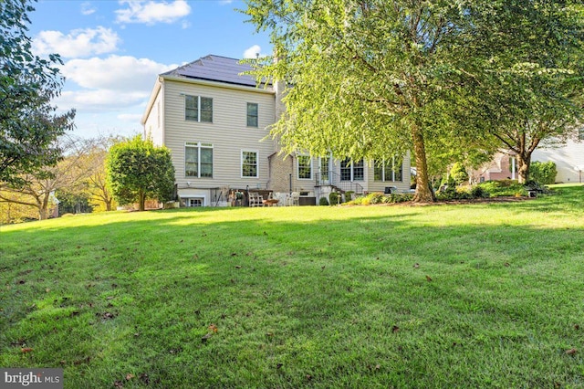 rear view of house featuring solar panels and a lawn