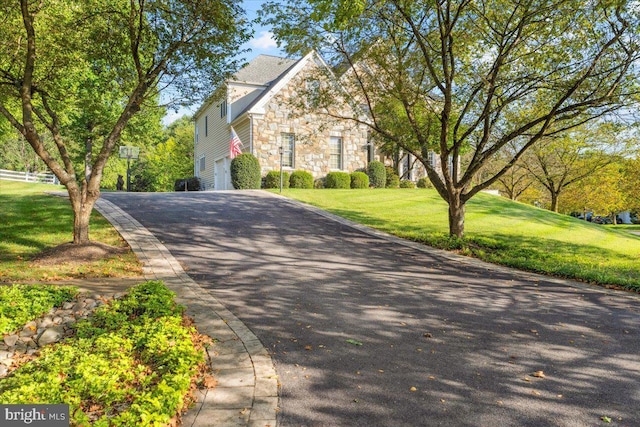 view of front of home featuring a garage, stone siding, aphalt driveway, and a front yard