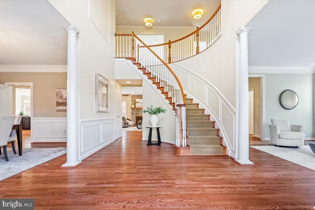 entrance foyer with decorative columns, ornamental molding, and wood finished floors