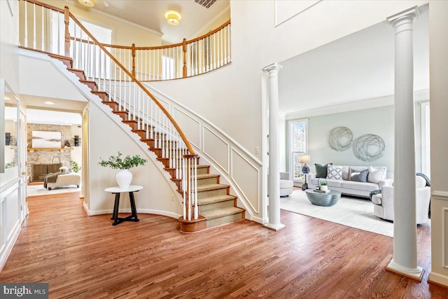 foyer featuring decorative columns, stairway, wood finished floors, a high ceiling, and crown molding