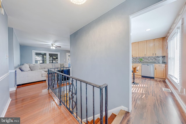 corridor with light wood-type flooring, visible vents, baseboards, and an upstairs landing