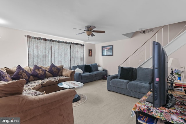 carpeted living room featuring ceiling fan and stairway