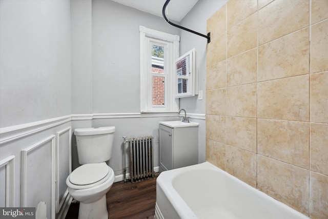 full bathroom with radiator, toilet, wood finished floors, vanity, and a decorative wall