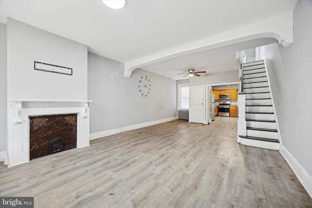 unfurnished living room featuring a fireplace, light wood finished floors, radiator, stairway, and baseboards