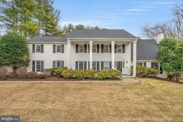 greek revival inspired property featuring roof with shingles, a chimney, and a front lawn