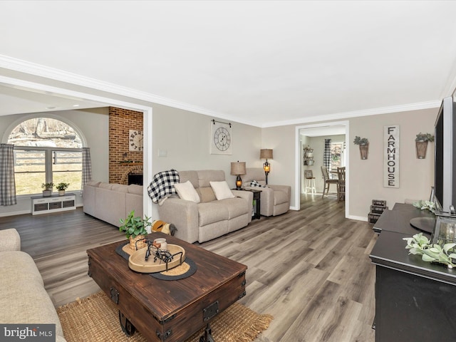 living area with light wood-style floors, a brick fireplace, baseboards, and crown molding