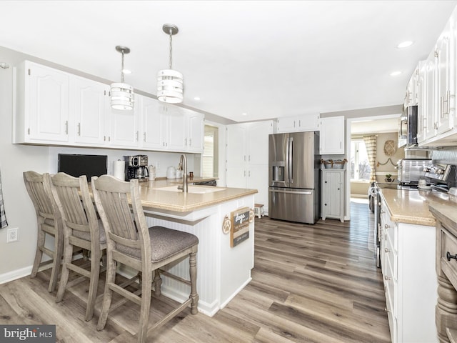 kitchen featuring white cabinets, light wood-style flooring, appliances with stainless steel finishes, and a kitchen breakfast bar