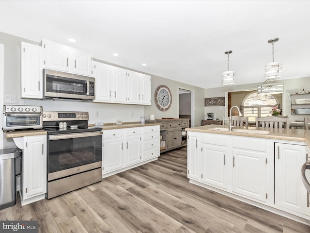 kitchen with stainless steel appliances, light countertops, light wood-style flooring, white cabinetry, and a sink