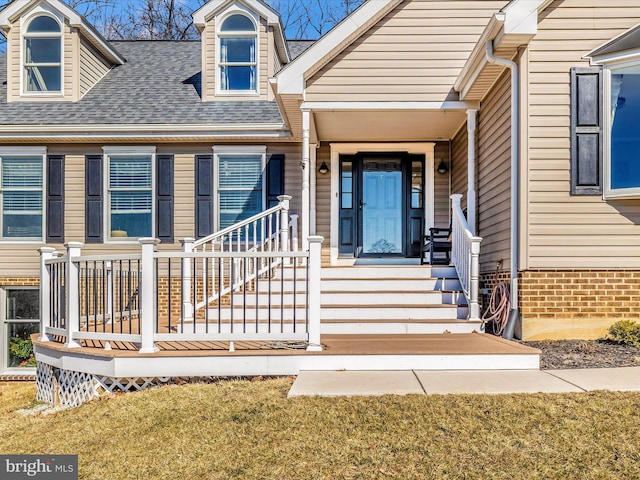 doorway to property featuring a shingled roof and a lawn