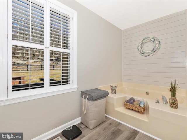 bathroom with wood finished floors, wood walls, baseboards, and a bath