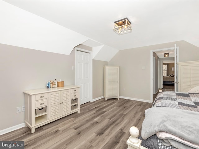 bedroom with light wood-style floors, vaulted ceiling, and baseboards