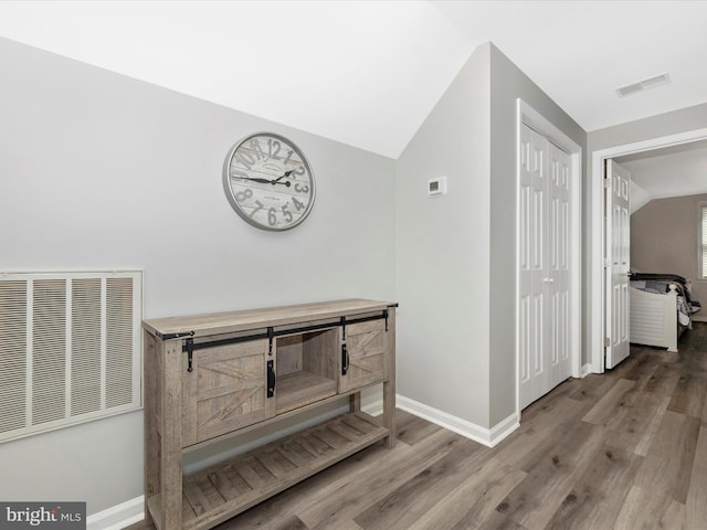 hall featuring lofted ceiling, baseboards, visible vents, and wood finished floors