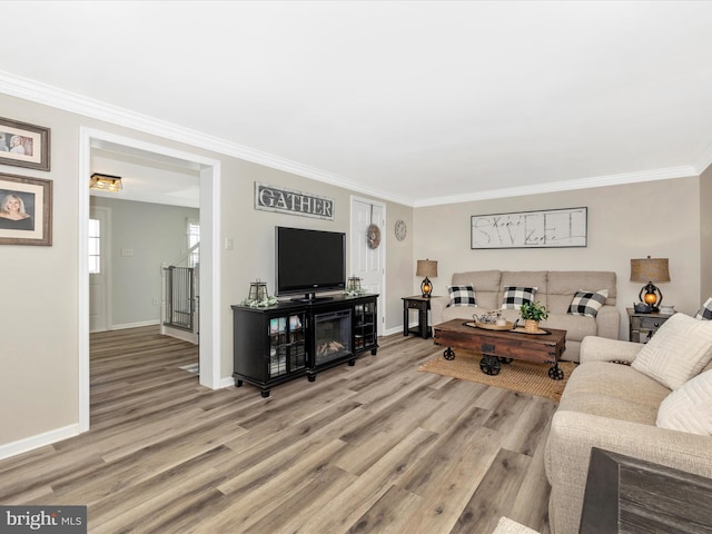 living room featuring light wood-type flooring, baseboards, stairway, and crown molding