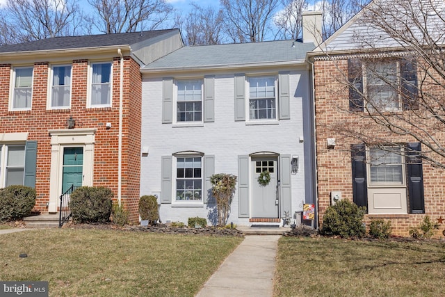 view of property with brick siding, a chimney, and a front yard