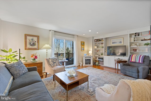 living room with a glass covered fireplace, recessed lighting, wood finished floors, and built in features