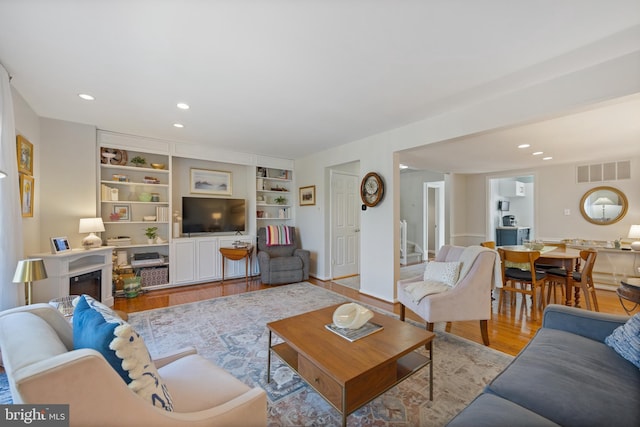 living area featuring recessed lighting, visible vents, wood finished floors, and a glass covered fireplace