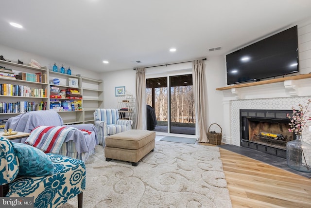 living area with recessed lighting, visible vents, a tiled fireplace, and wood finished floors