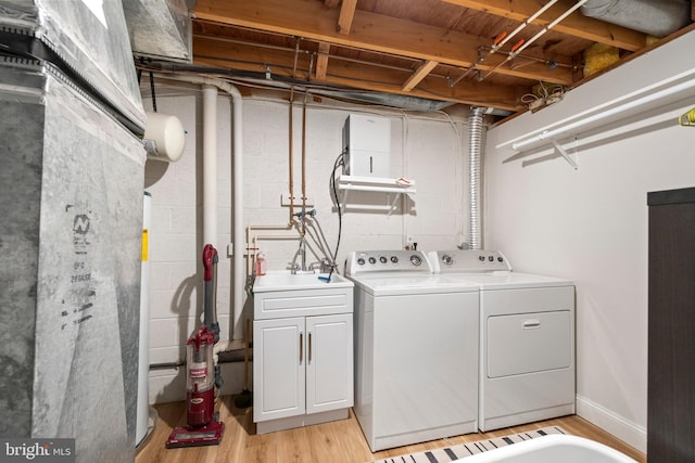 laundry room featuring light wood-type flooring, baseboards, washer and clothes dryer, and a sink