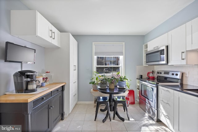 kitchen featuring light tile patterned flooring, white cabinetry, baseboards, appliances with stainless steel finishes, and decorative backsplash