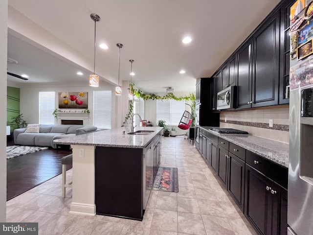 kitchen featuring decorative light fixtures, a center island with sink, appliances with stainless steel finishes, open floor plan, and a kitchen breakfast bar