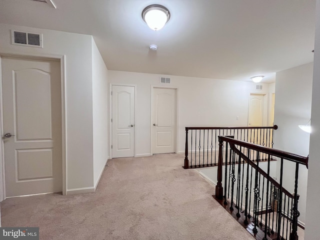 hall with light carpet, baseboards, visible vents, and an upstairs landing