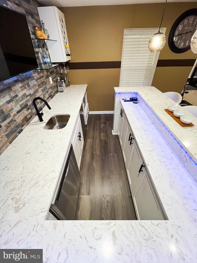 kitchen with decorative light fixtures, stainless steel dishwasher, white cabinets, a sink, and light stone countertops