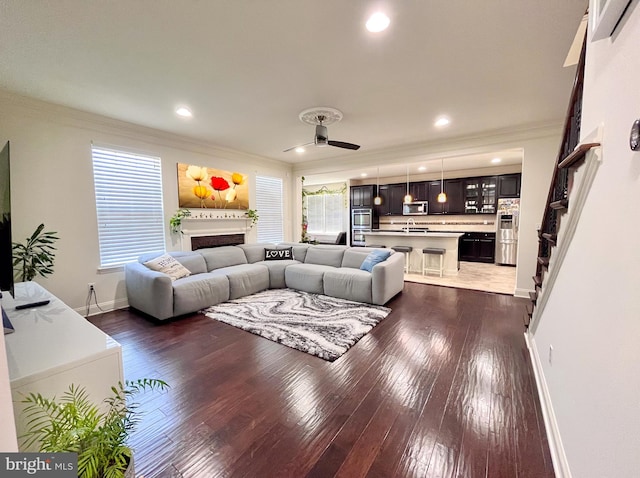 living area featuring ceiling fan, a fireplace, baseboards, dark wood finished floors, and crown molding