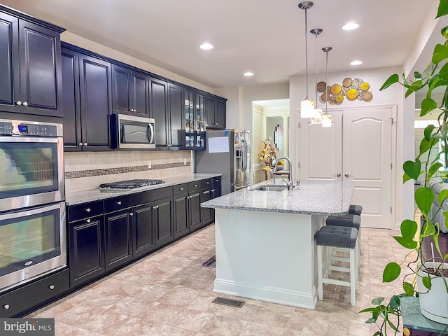 kitchen featuring glass insert cabinets, a breakfast bar, a kitchen island with sink, stainless steel appliances, and a sink