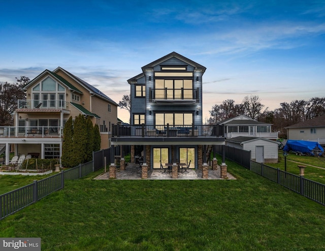 back of house at dusk featuring a patio area, a lawn, and a fenced backyard