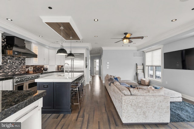 kitchen with premium appliances, open floor plan, wall chimney exhaust hood, tasteful backsplash, and crown molding