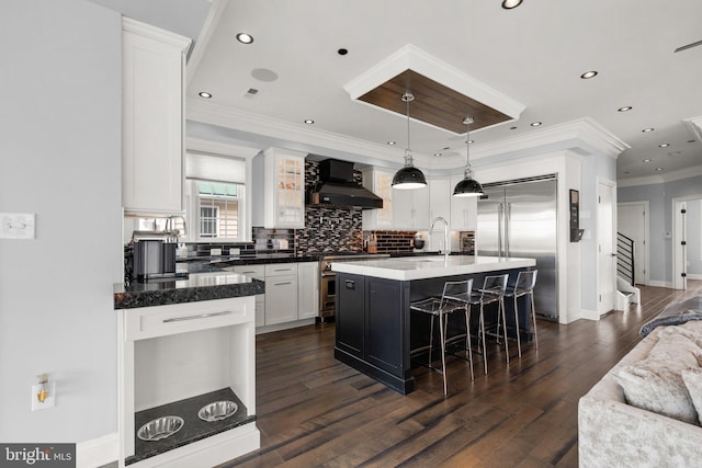 kitchen with a sink, white cabinets, wall chimney range hood, decorative backsplash, and high end appliances